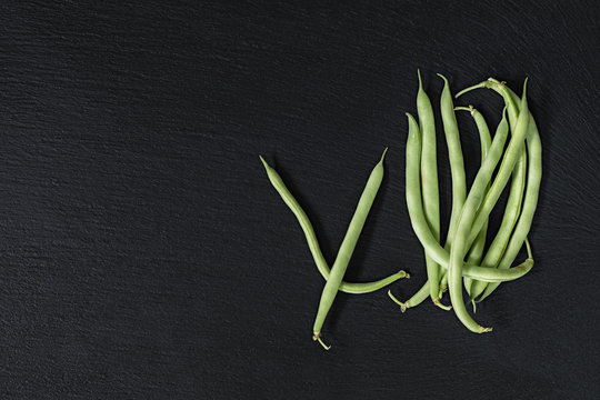 Pods fresh green beans on a black stone surface.  Top view, copy space. Healthy eating concept.