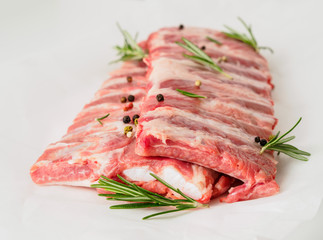 raw pork ribs with seasoning  rosemary, pepper on white parchment paper, side view