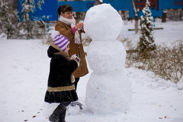 Happy grandmother and granddaughter sculpt a big snowman, Happy family play in a winter park