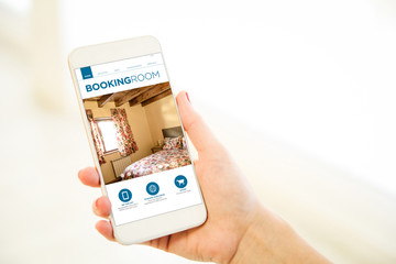 Woman holding a pink gold blank smartphone showing booking room website