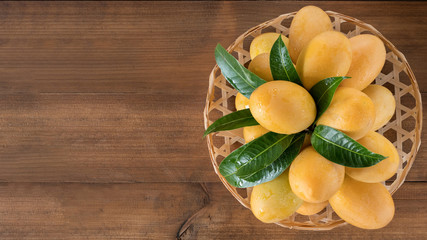 Sweet Marian plum in a bamboo basket on wooden table, concept of tropical fruits