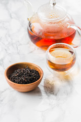 Dry tea in wooden plate and glass cup of tea on marble background