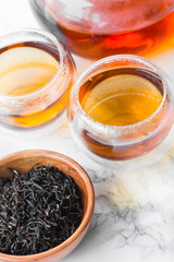 Dry tea in wooden plate and glass cup of tea on marble background