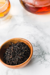 Dry tea in wooden plate and glass cup of tea on marble background