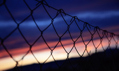 Wire mesh fence on silhouettes of poles on sky blur background at sunset