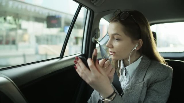 Businesswoman Putting on Lip Gloss in the Moving Car