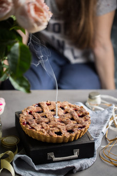 A birthday cherry cake with a burning one white candle. Atmospheric beautiful food birthday photo with home cherry pie, flowers, ribbons and decoration.