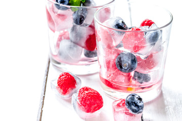 glass with frozen berries in cubes on wooden desk background