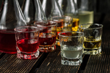 Assorted alcoholic cordials in glasses and decanters on dark wood background