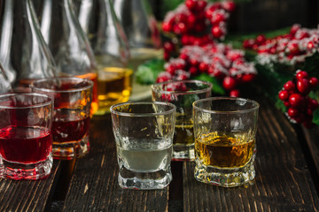 Assorted alcoholic cordials in glasses and decanters with Christmas decorations on dark wood...