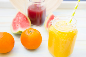 Fresh Tropical Smoothie Concept. Glass jar of fruit and berry smoothie, whole orange and sliced watermelon on a light wooden table against a wooden plate