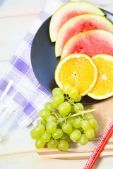 Fresh Tropical Fruit, Healthy Diet Concept. Fresh fruit on the black plate: sliced watermelon, orange and a bunch of green grapes on a black plate, light table with napkin