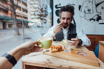 Happy and loving hipster millennial couple, shares lunch or brunch at morning trendy cafe or coffeeshop, drink latte or espresso, eat sweet dessert, easy going lifestyle of freelancers or bloggers