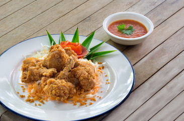 Fried chicken wing stick with coating flour in white dish and sweet chicken sauce on brown wooden...
