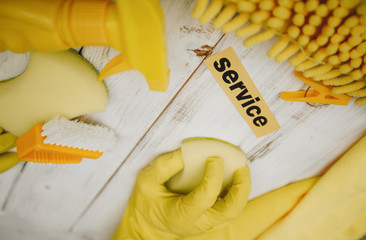 Cleaning Concept. Yellow cleaning supplies: sponges, brush, and sprayer, a hand in a rubber glove...