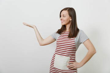 Young attractive smiling brunette caucasian housewife in striped apron isolated on white background. Beautiful housekeeper woman pointing hand aside looking aside. Copy space for advertisement.
