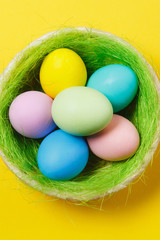 Vertical six colorful pastel painted Easter eggs in basket with green grass isolated on yellow background. Happy Easter concept. Copy space for advertisement. With place for text. Top view on eggs.