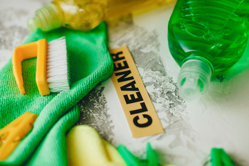 Set of yellow and green cleaning tools: rags, brushes, clothes peg and dishwashing liquid on light concrete background with cleaner inscription, top view, flat lay