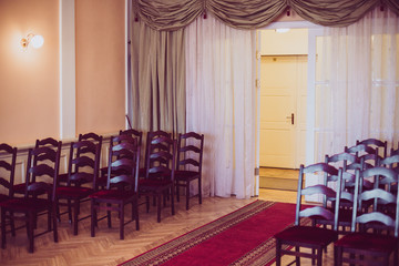 Marriage Registry Hall with red carpet. Brown wooden chairs are put together in a row. Vintage effect.