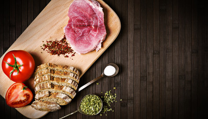 raw meat with tomato and bread and special on spoons on a black wooden background