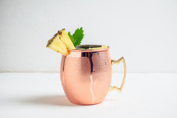 Cold pineapple Moscow Mule cocktail in copper mug on the rustic background. Shallow depth of field.
