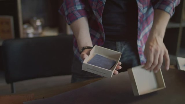 Man hands packaging product in cardboard box. Worker put leather wallet in product packaging box in small shop. Craftsman putting handmade product in cardboard box