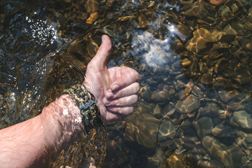 Human hand with military watch touching mountain river water. feel it, crisal clean