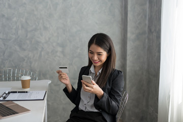 Fototapeta premium Asian business girl in her workstation buying online with a credit card and smart phone. Online shopping Concept.
