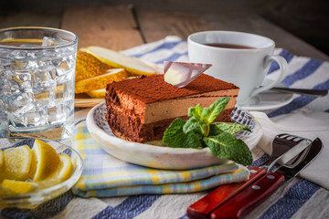 Chocolate cake and a cup of tea; water with ice and slices of pear; on background.