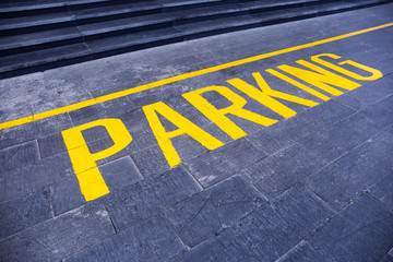 the word "parking" painted in yellow on gray asphalt