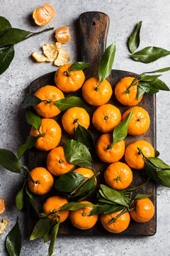 Tangerines with green leaves on wooden board on light background