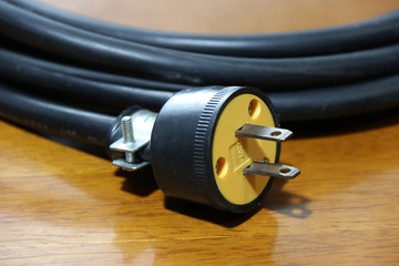 Yellow plug with black cable on the wooden floor. Used for electrical connection. Long distance between the outlet of electric and electric equipment.