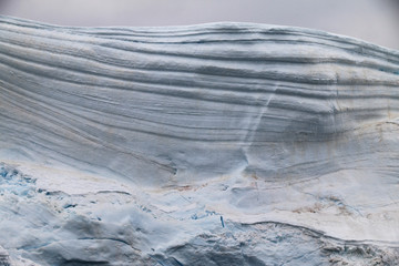 warstwy śniegu i lodu w odłamanym fragmencie góry lodowej z szarym niebem w tle