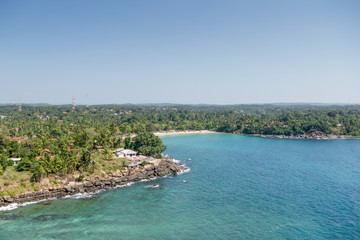 Sri Lanka. Dondra. Top view from the lighthouse to the turquoise sea (ocean), rocky beach, sandy beach, green palms, red tiled roofs of houses and boats on the jig.