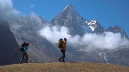 Hikers with backpacks travel in the Himalayan mountains. They look at the snowy peaks and are happy with the trip. 4K