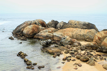 Large brown stones (boulders) on the seashore (ocean), sandy beach, waves