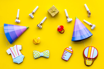 Celebrate child's birthday. Cookies in shape of baby accesssories, party hats, gift box on yellow background top view