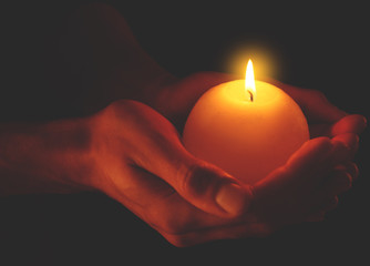 Young man holding burning candle in darkness
