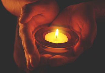 Young man holding burning candle in darkness