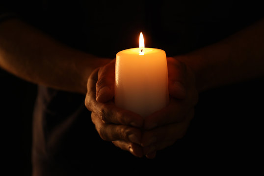 Young man holding burning candle in darkness