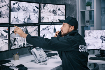Male security guard using radio transmitter in surveillance room