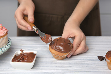 Female baker decorating tasty cupcake with chocolate cream at table