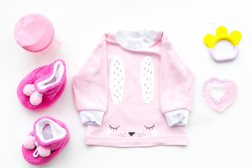 Cute pink baby clothes for girl. Shirt, booties, toy, bottle on white background top view copy space