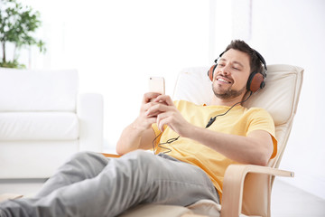 Young man listening to music while relaxing in armchair at home