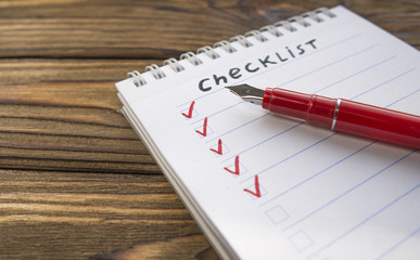 checklist, red pen on the background of a wooden table. close-up