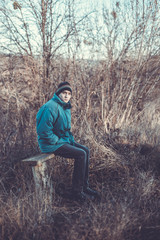 A young man sits on an old bench in the countryside in the autumn time.