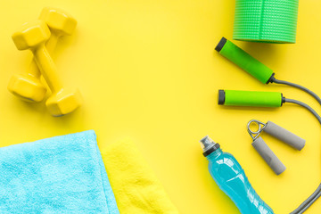 Fitness background. Equipment for gym and home. Jump rope, dumbbells, expander, mat, water on pastel yellow background top view space for text