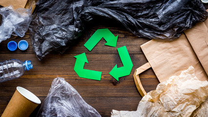 Green paper recycling sign among waste materials paper, plastic, polyethylene on dark wooden...