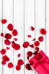 Gift for Valentine's day. Red gift box near red rose petals on white wooden background top view copy space