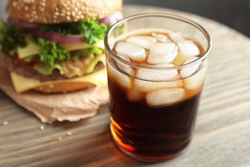 Glass of cold cola with tasty burger on table